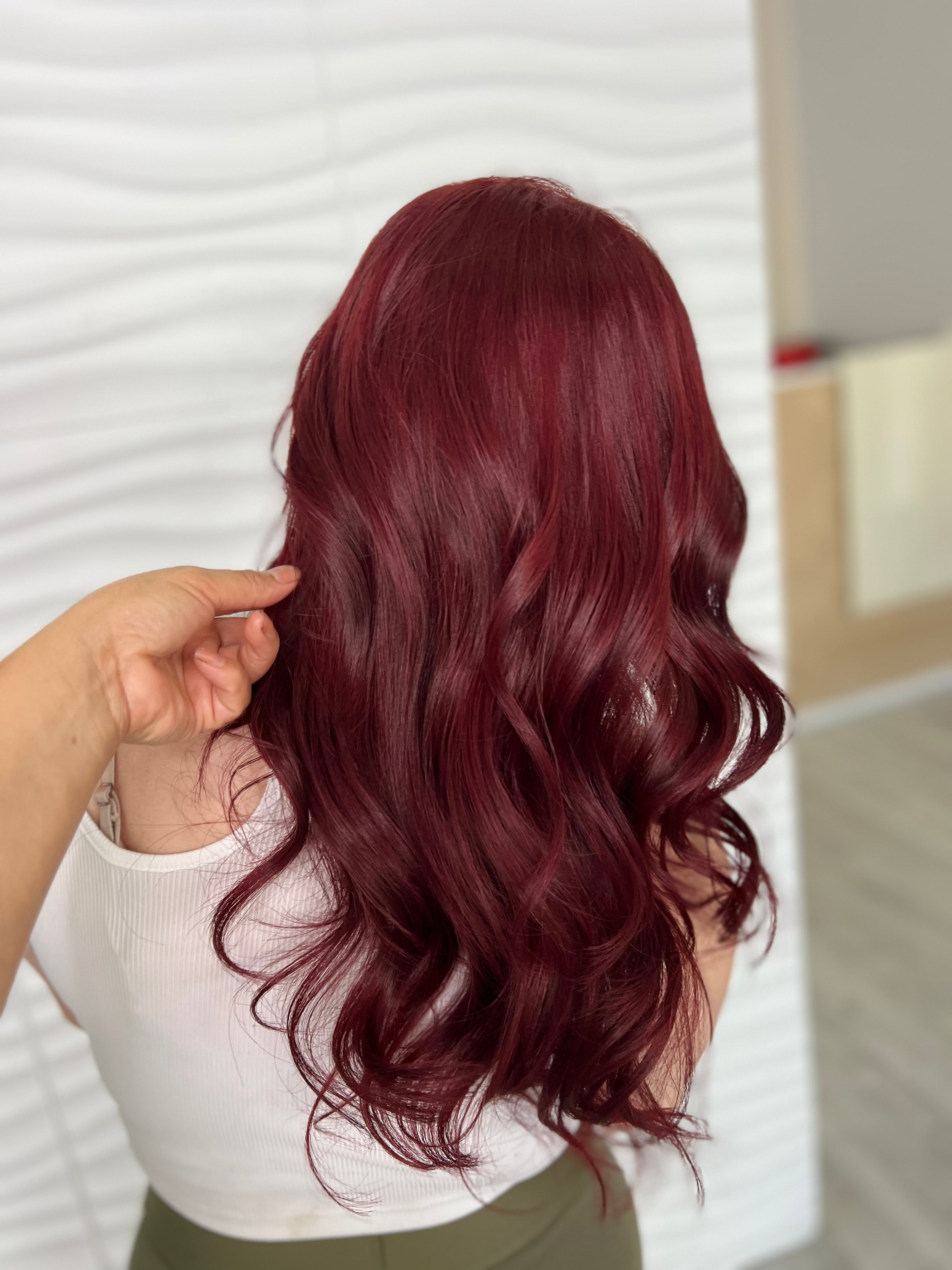 Persona con cabello largo, ondulado y rojo contra una pared blanca.